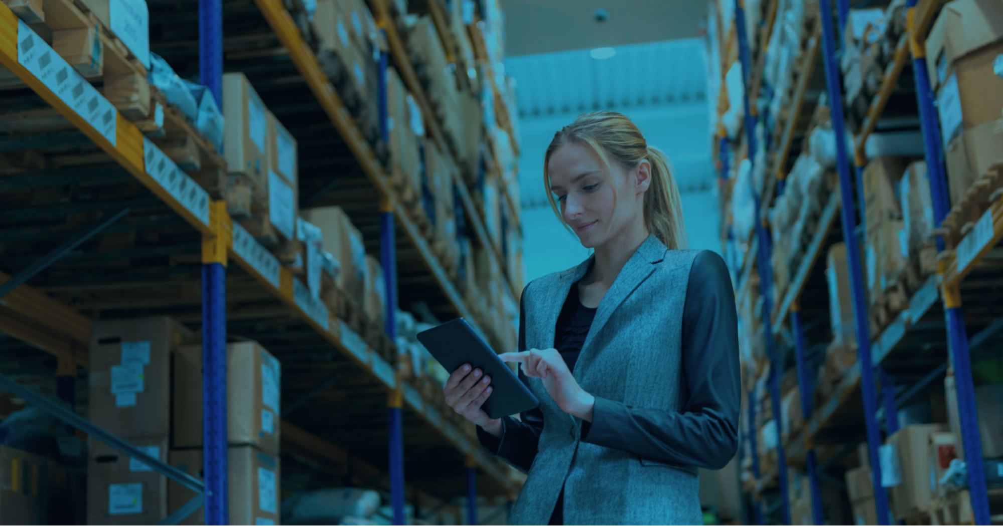 A woman checking a digital tablet in a warehouse setting.