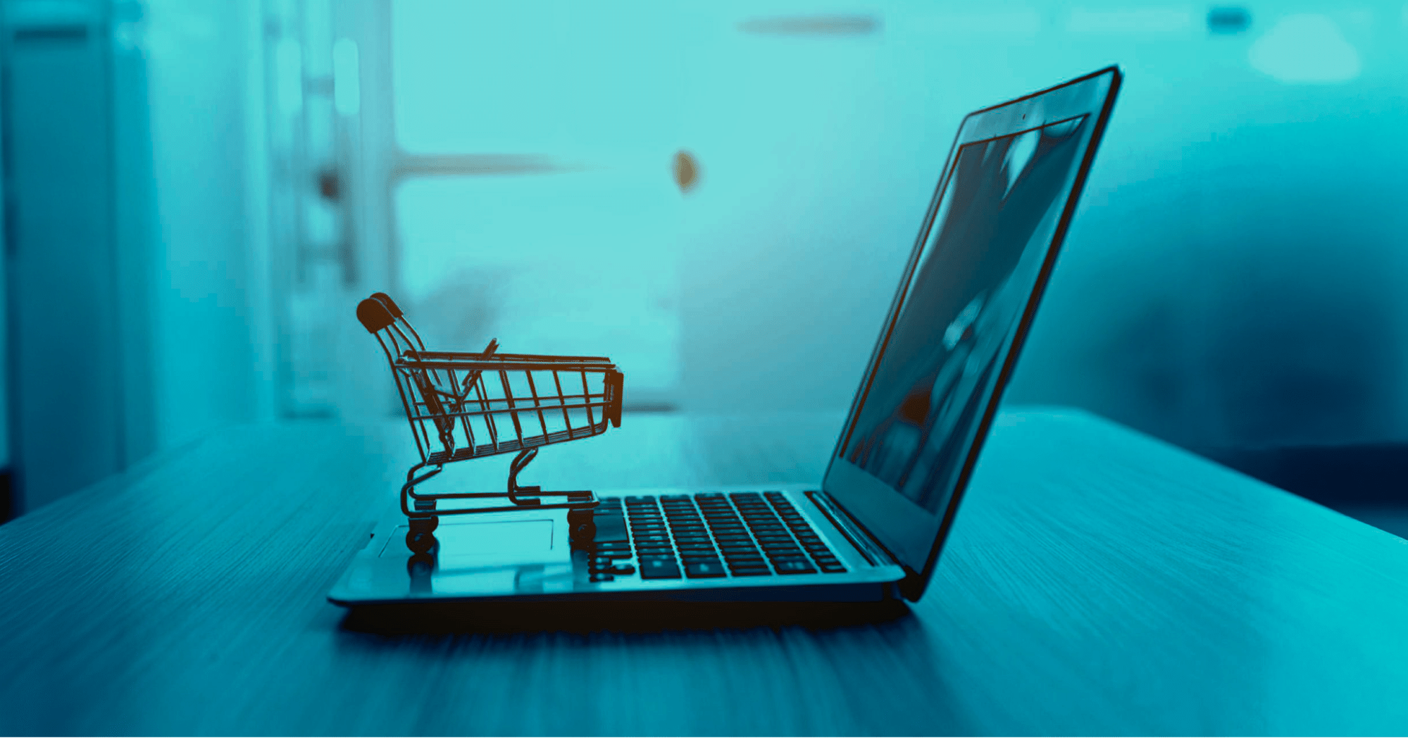 A miniature shopping cart sits on the keyboard of an open laptop.